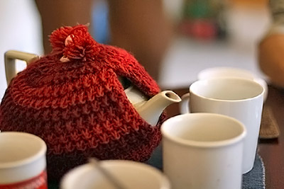 A photographic image of a teapot with a red cozy.