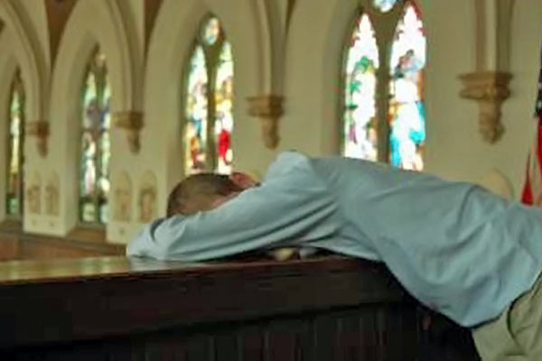 A photographic image of a man praying in a church.