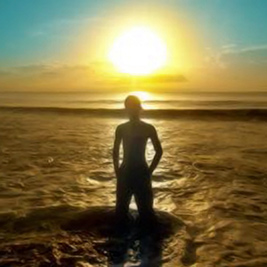 A photographic image of a young man at the seashore gazing at the sunrise.