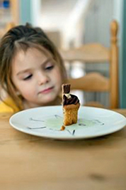 A photographic image of a girl tempted by a sliver of cake.