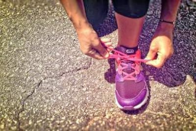 A photographic image of hands tying a pink athletic shoe.