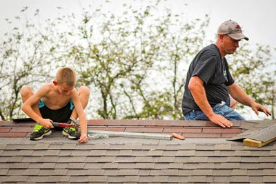 A photographic image of a father and son repairing a roof